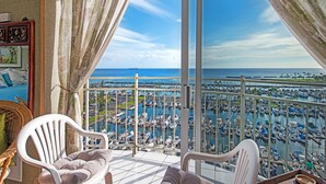 Un balcon donnant sur une marina remplie de bateaux, avec un navire visible au loin et une chaise.