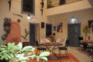 Un interior tradicional con techo alto, puertas ornamentales y una mesa redonda central con sillas.