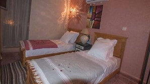 A bedroom with two single beds, a nightstand with a lamp, and an air conditioning unit mounted on the wall. - Riad belko - Hostel (Marrakech)