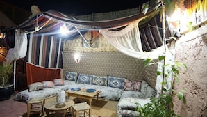 An outdoor seating area with a sofa, chairs, and a table, surrounded by draped fabric and a patterned wall. - Riad belko - Hostel (Marrakech)