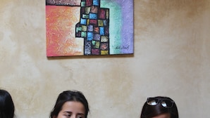 Three people sitting on a patterned couch with a colorful abstract painting on the wall behind them. - Riad belko - Hostel (Marrakech)