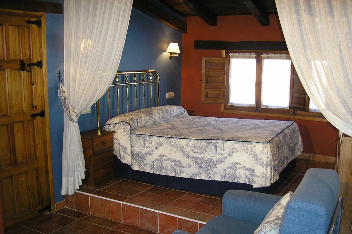 Een slaapkamer met een bed, een stoel, een raam en gordijnen.