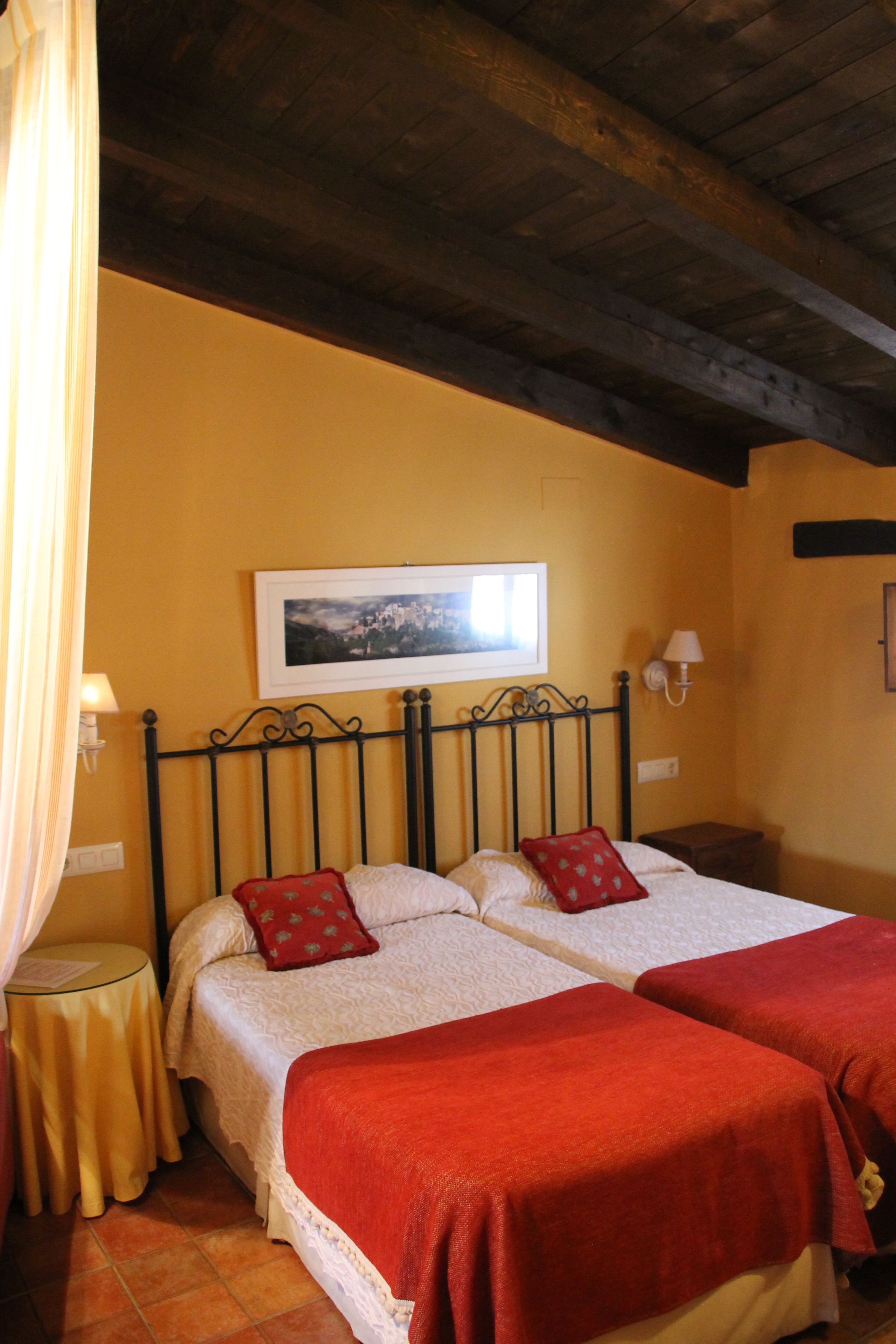 A double bed with red bedding, a small bedside table, a lamp, and a framed picture on the wall.