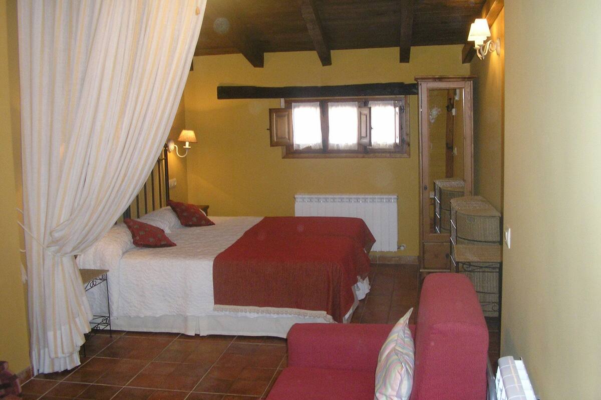 Een slaapkamer met een bed, een rode bank, een raam en een radiator.