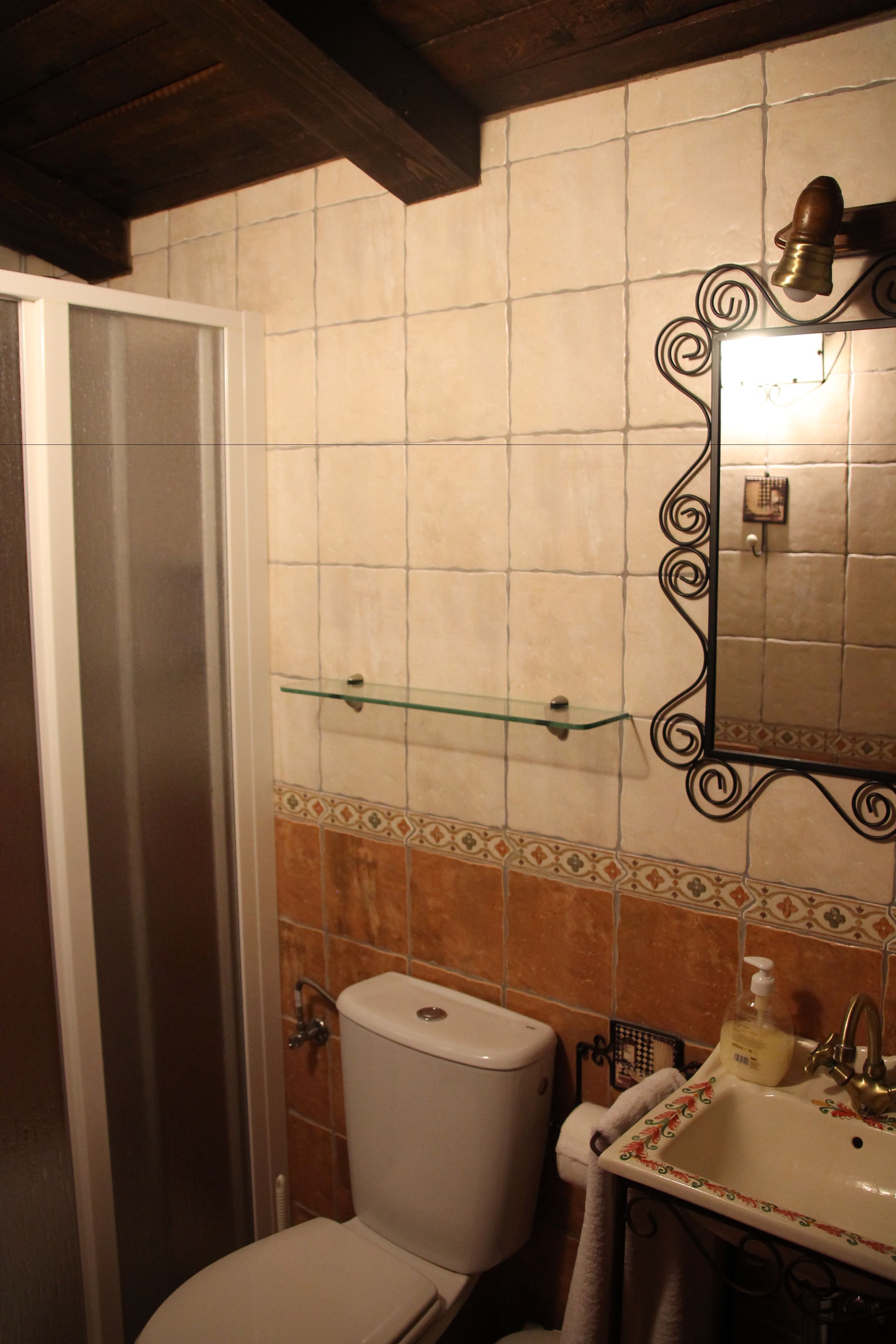 A bathroom with a toilet, a glass shelf above the sink, and a mirror with a decorative frame.