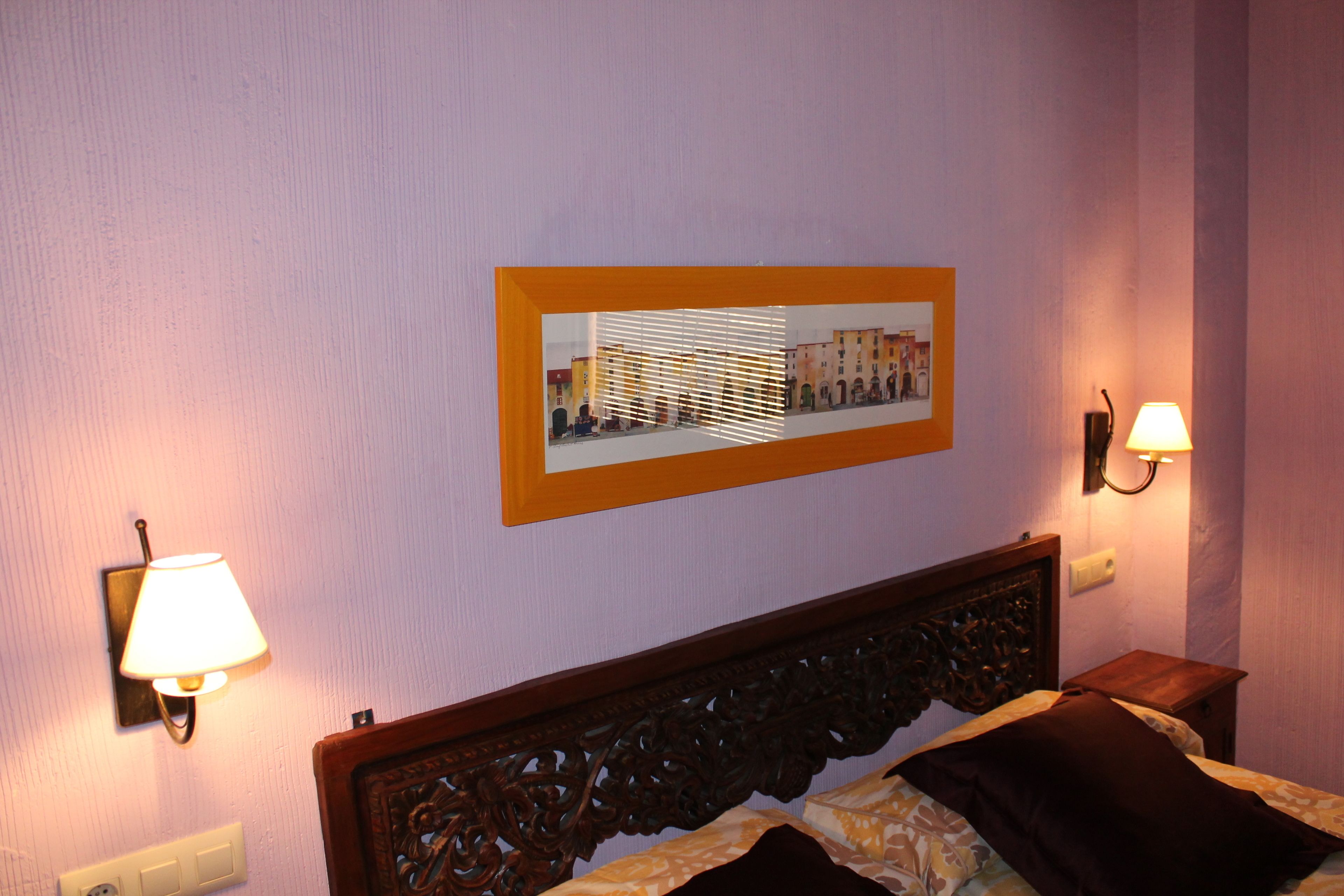 A hotel room with a bed, a headboard, a wall-mounted picture, and two wall sconces.