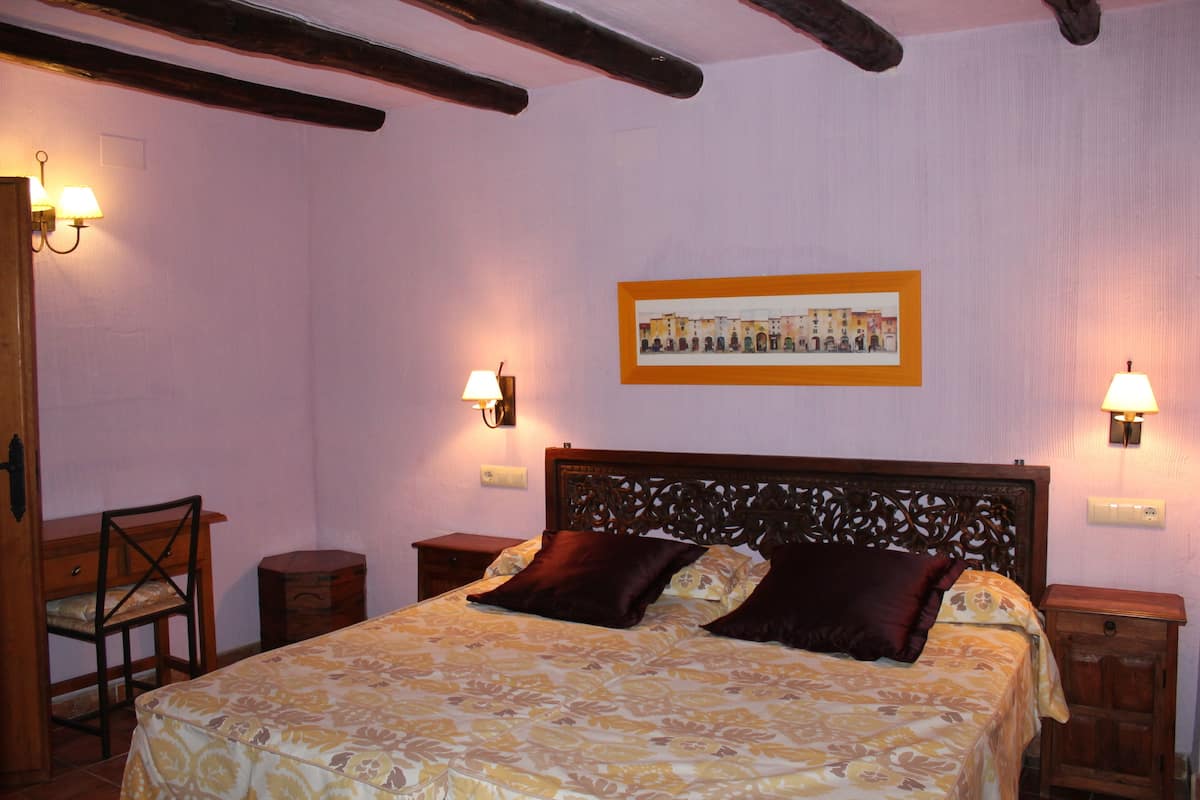 Een slaapkamer met een bed, een houten hoofdbord, twee nachtkastjes, een stoel en een lijst met een afbeelding aan de muur.