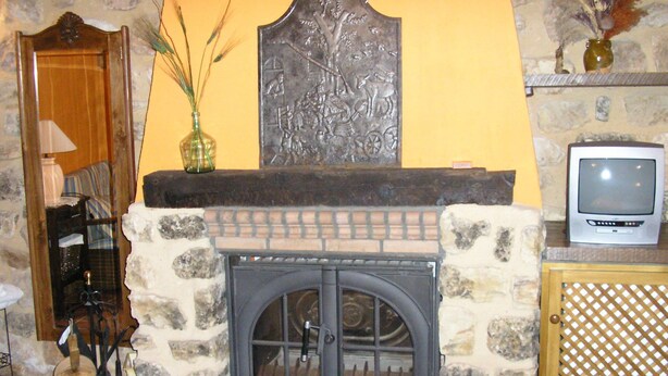 Une cheminée en pierre surmontée d’une plaque métallique décorative, un téléviseur posé sur une étagère à droite et une porte en bois à gauche.