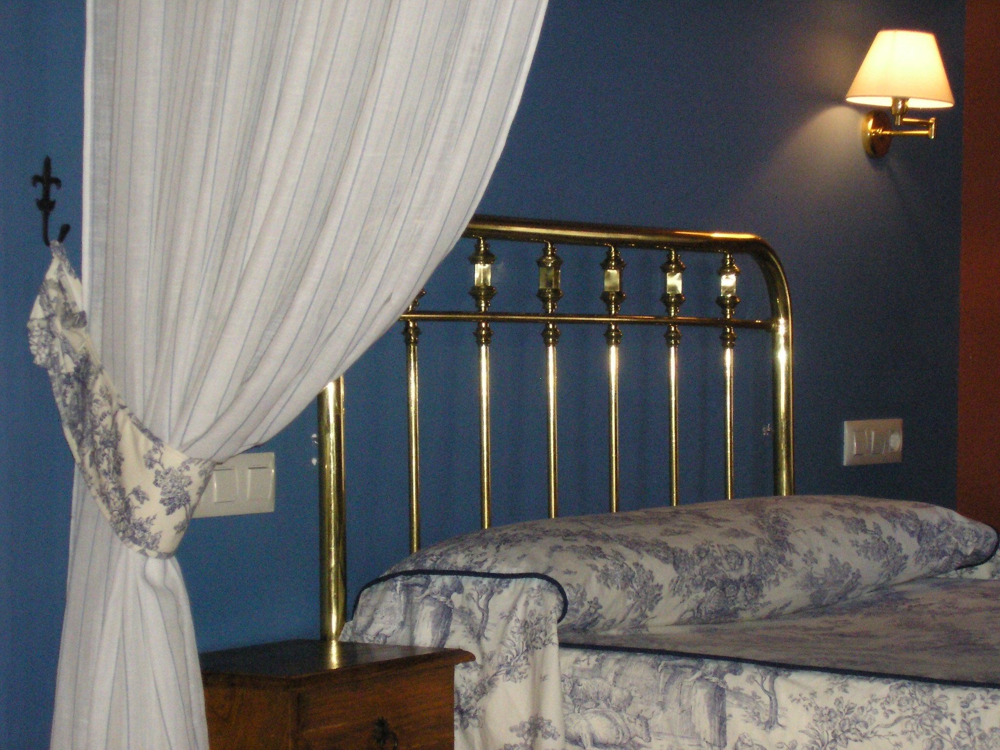 A bed with a metal headboard, a bedside table, and a wall-mounted lamp.