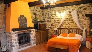 Une chambre aux murs de pierre, équipée d’un lit, d’une cheminée et d’un téléviseur.
