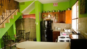 Une cuisine avec des murs verts, une table à manger, des chaises, un réfrigérateur, une cuisinière et des armoires en bois.