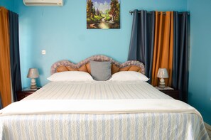 A bedroom with a bed, two bedside tables, a wall-mounted air conditioner, and a painting of a landscape.