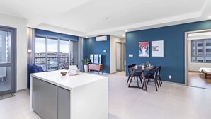 A modern kitchen with a central island, a dining area with a table and chairs, and a living area with a sofa and a TV.
