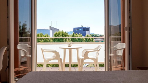 A balcony with a table and chairs, a view of a building with a sign, and a clear sky. - Hotel Silvia (Castello d'Empuries)