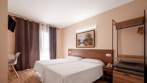 A hotel room with two beds, a desk, a chair, a coat rack, and a painting on the wall. - Hotel Silvia (Castello d'Empuries)