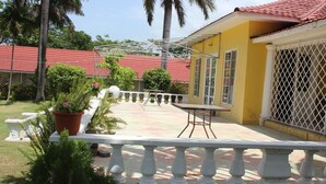 A yellow building with a red roof, a covered patio area with a table and chairs, and a white railing. - Villa Loyola (Ocho Rios)