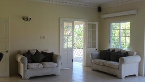 A spacious living room with two white sofas, a ceiling fan, and large windows providing natural light. - Villa Loyola (Ocho Rios)