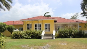 A yellow building with a red roof, a staircase leading to the entrance, and a well-maintained lawn with tropical plants. - Villa Loyola (Ocho Rios)