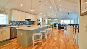 A spacious kitchen with a large island, white cabinetry, and a bar area with stools.