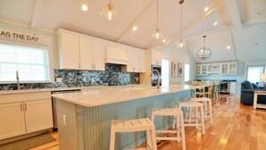A spacious kitchen with a large island, white cabinets, and a blue backsplash. There are bar stools and a chandelier.