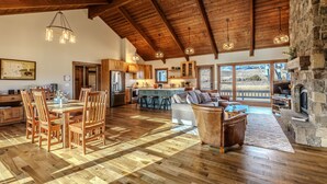 A spacious living area with a wooden ceiling, a stone fireplace, and a large window overlooking a scenic landscape.