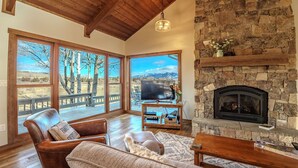 A cozy living room with a stone fireplace, leather sofas, and large windows offering a scenic view.