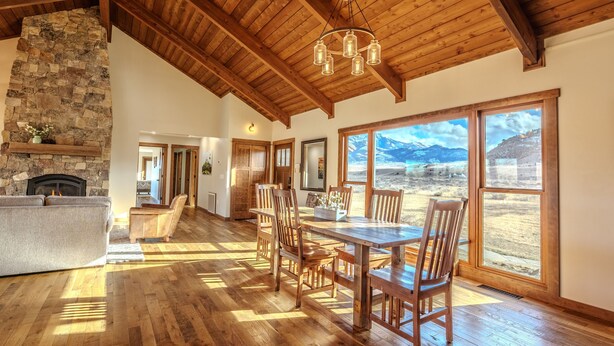A spacious living room with a stone fireplace, wooden dining table, and large windows offering a mountain view.