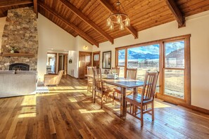 Cozy living area with a stone fireplace, comfortable sofa, and dining table, offering a view of the surrounding mountains.