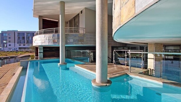 En swimmingpool med klart vand, en træterrasse og en bygning med balkon.