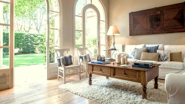 Ein geräumiges Wohnzimmer mit einem großen Bogenfenster, einem weißen Sofa, einem Holztisch und einem weißen Teppich.