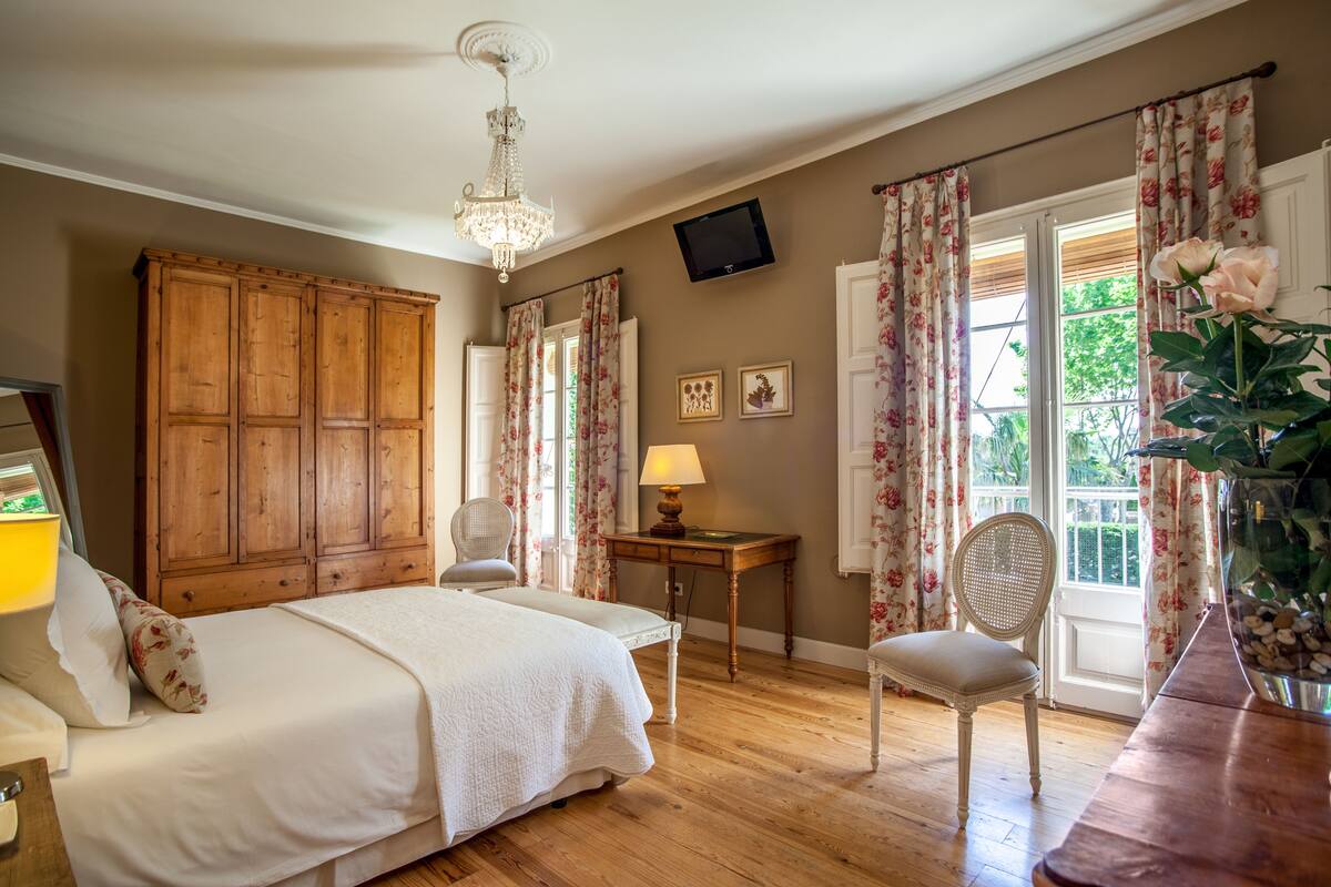 Un dormitorio con un armario de madera, una cama con ropa de cama blanca, un escritorio con lámpara y una silla.