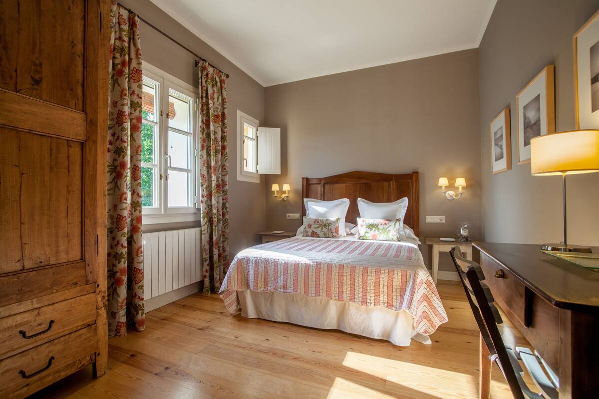 Un dormitorio con un armario de madera, una cama con ropa de cama floral, dos lámparas de noche y una mesita de noche.