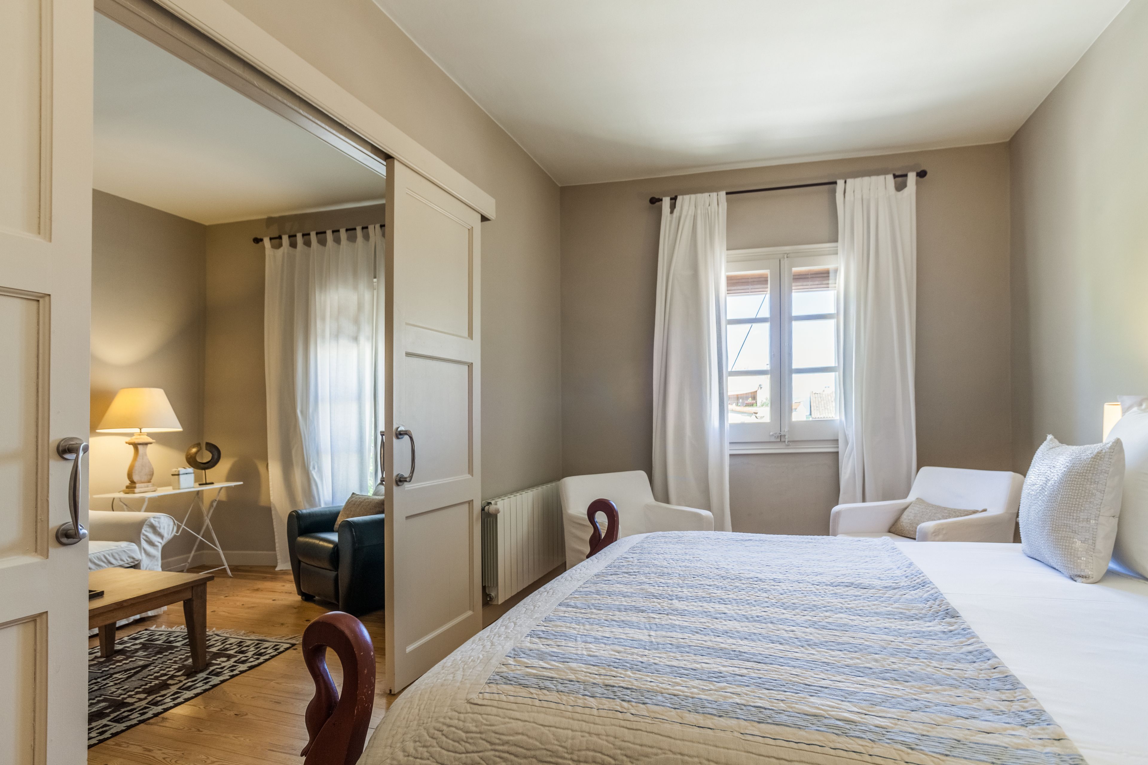 A hotel room with a bed, a chair, a table, and a window with curtains.