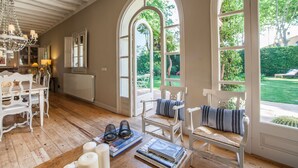 Ein geräumiges Zimmer mit Holzboden, weißen Möbeln und großen Fenstern mit Blick auf den Garten.