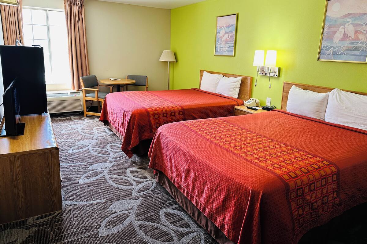 A hotel room with two beds, a desk with a TV, a chair, a lamp, and two paintings on the wall.