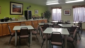 Un espace repas avec des tables et des chaises, un comptoir avec une machine à café et une grande fenêtre avec des rideaux.