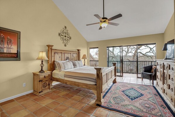 A bedroom with a bed, nightstands, a ceiling fan, a window, and a balcony with a chair.