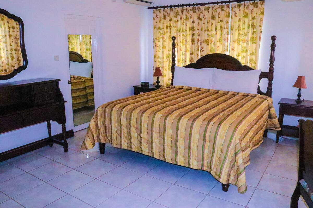 A bedroom with a large bed, a dresser, a mirror, and a window with curtains.