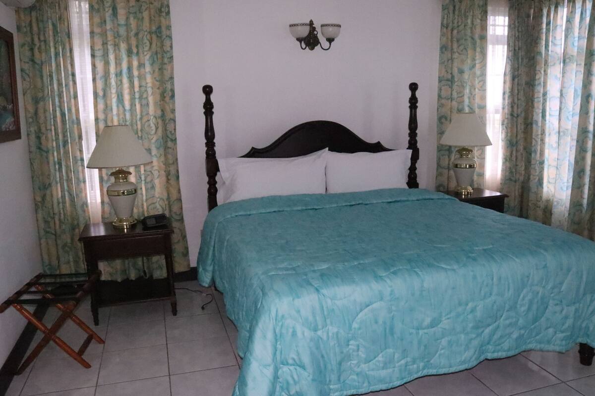 A bedroom with a bed, two bedside tables with lamps, a wall-mounted light fixture, and curtains.