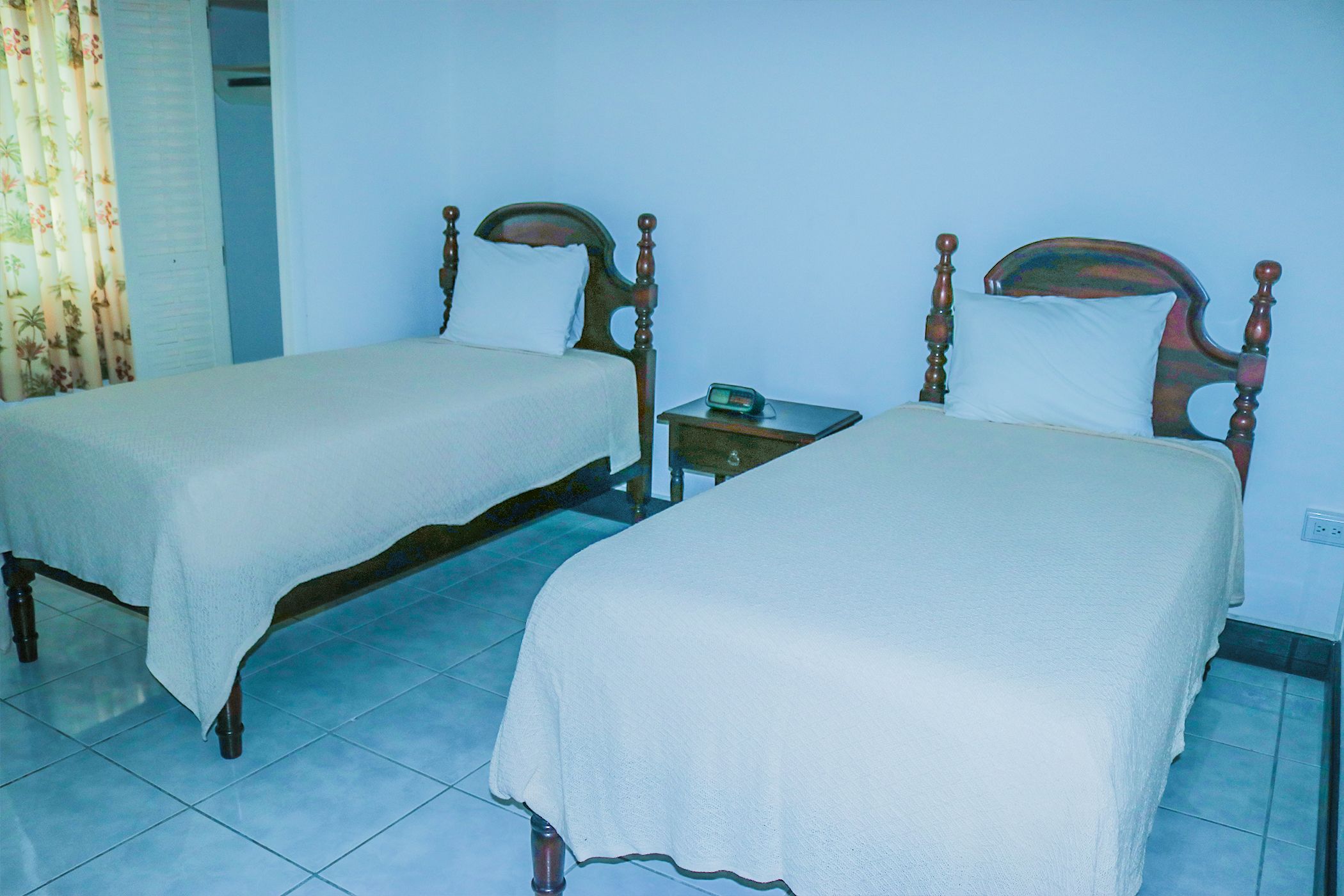 Two single beds with wooden frames and white bedding in a room with tiled flooring.