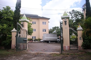 A gated entrance with a truck parked inside, a building with a beige facade, and a paved driveway leading to the entrance. - Royal Tower Suites (Tower Isle)