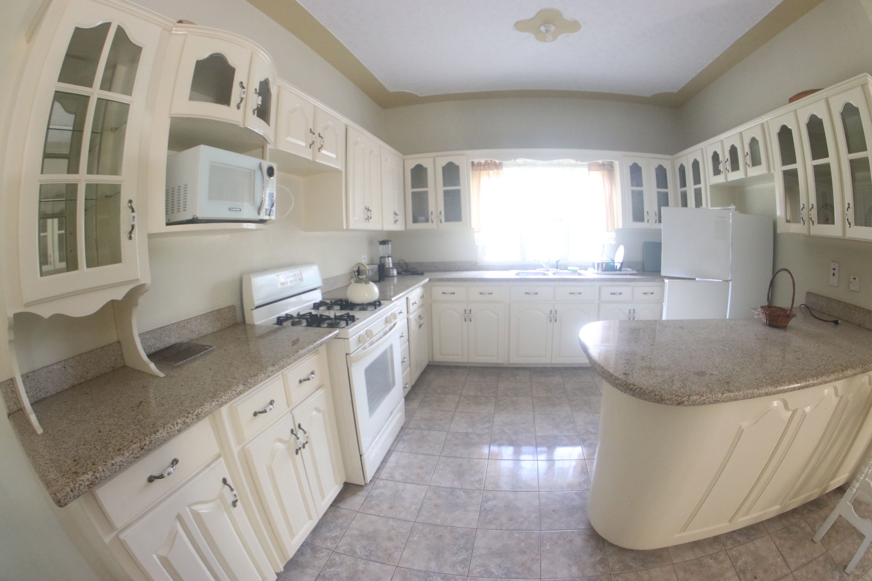 Una cocina con gabinetes blancos, estufa, microondas y refrigerador.