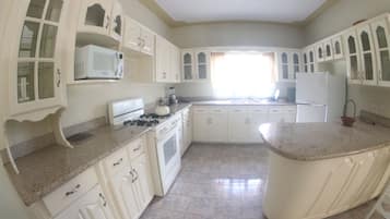 Una cocina con gabinetes blancos, estufa, microondas y refrigerador.