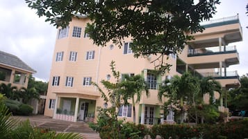 A multi-story building with a flat roof, balconies, and a garden area with red flowers.