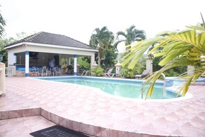 A swimming pool with a tiled deck, a covered seating area, and palm trees in the background. - Royal Tower Suites (Tower Isle)