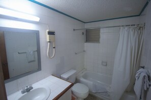 A bathroom with a toilet, sink, bathtub, and a shower curtain. - Royal Tower Suites (Tower Isle)