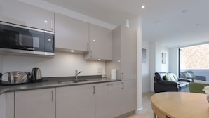 A modern kitchen with a Bosch microwave, a sink, and a toaster. There is a dining area with a table and chairs. - Fortified Apartment (Chelmsford)
