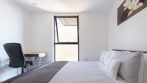 A modern hotel room with a bed, a desk, and a chair. - Fortified Apartment (Chelmsford)