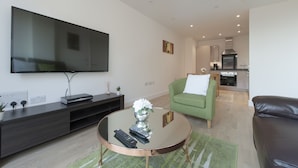 A modern living room with a flat-screen TV, a round coffee table, a green armchair, and a leather sofa. - Fortified Apartment (Chelmsford)