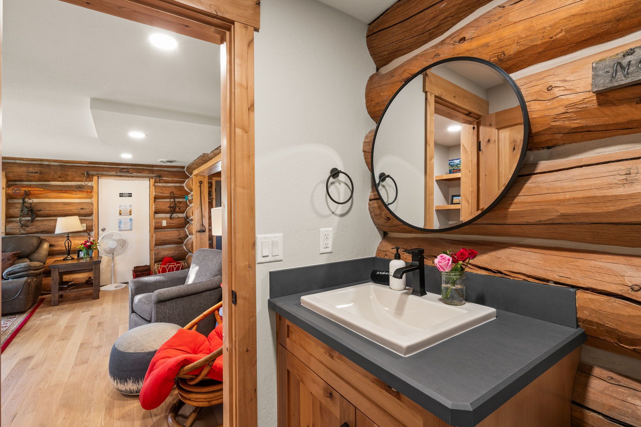 A modern bathroom with a wooden wall, a round mirror, and a white sink.